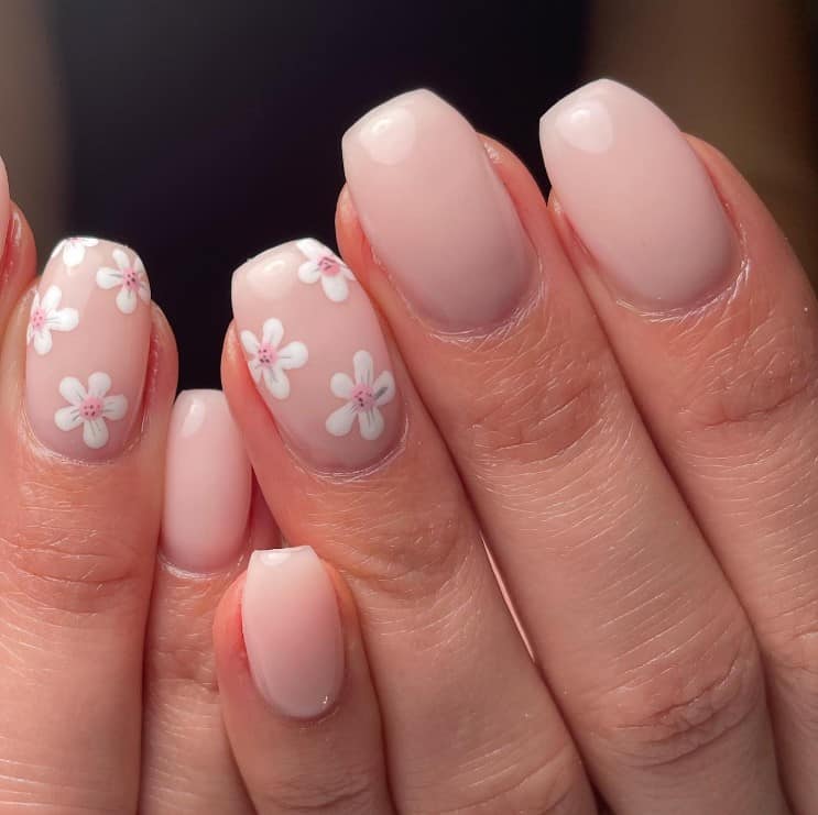 A closeup of a woman's fingernails with a nude nail polish that has cherry blossom art