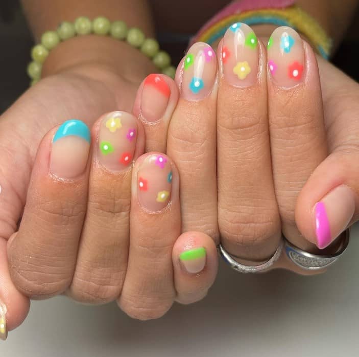 A closeup of a woman's fingernails with a nude nail polish that has multicolored flowers and French tips 