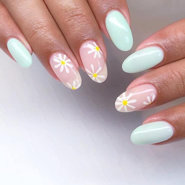 A closeup of a woman's fingernails with a combination of clear and light blue nail polish that has white and yellow flowers on clear nails 