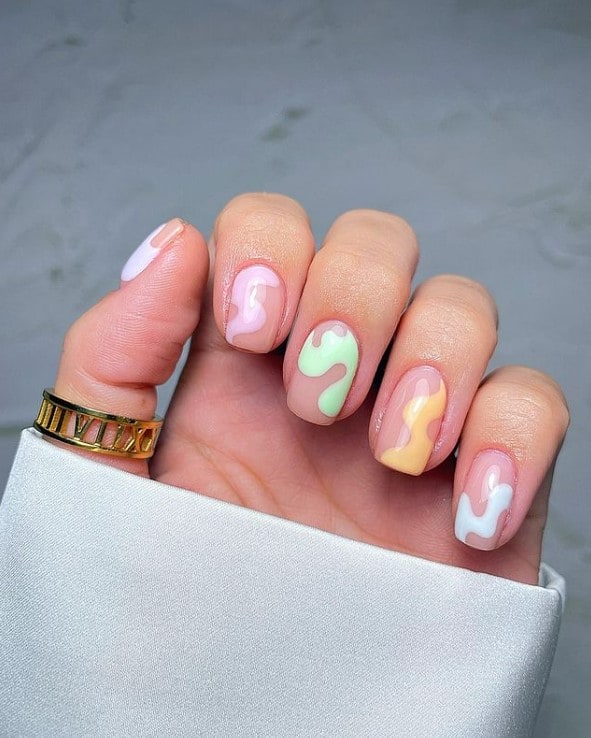 A woman's fingernails with a nude nail polish that has swirly design in soothing pastel shades