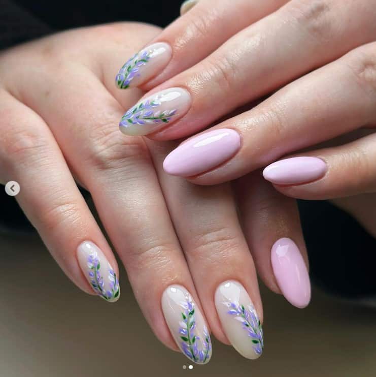 A closeup of a woman's oval shaped fingernails with a lavender nail polish that has lavender flowers