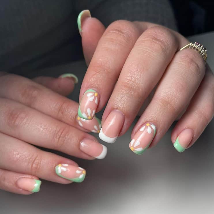 A closeup of a woman's fingernails with a nude nail polish that has mixing and matching French tips and flower art