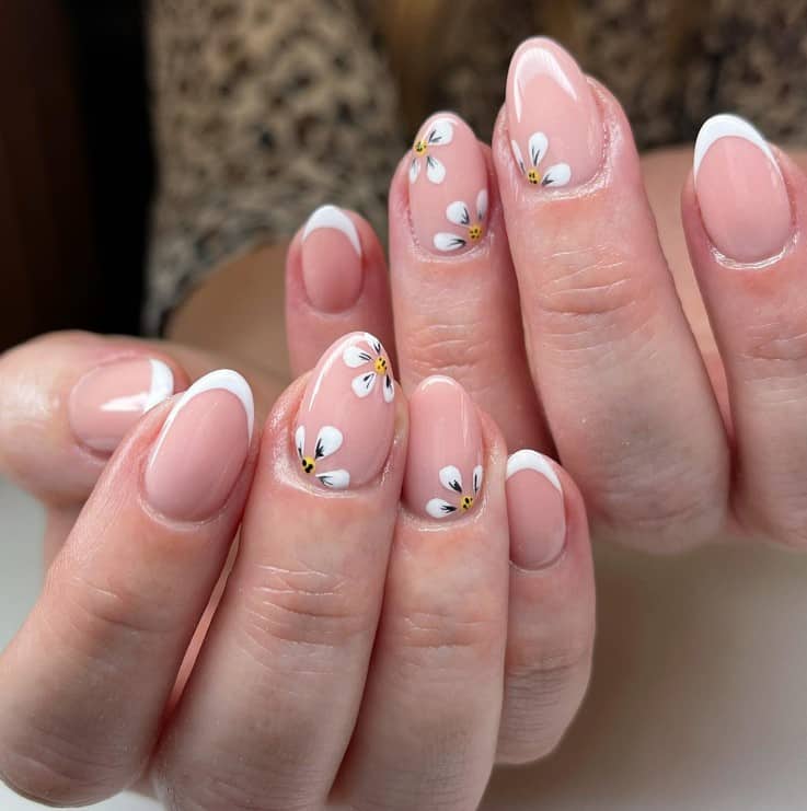 A closeup of a woman's fingernails with a nude nail polish base that has floral nail art 