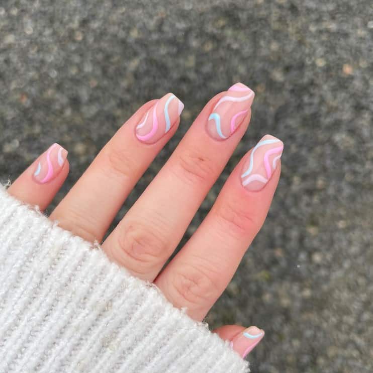 A woman's fingernails with a nude nail polish that has thin swirls in pink, purple, and blue polish