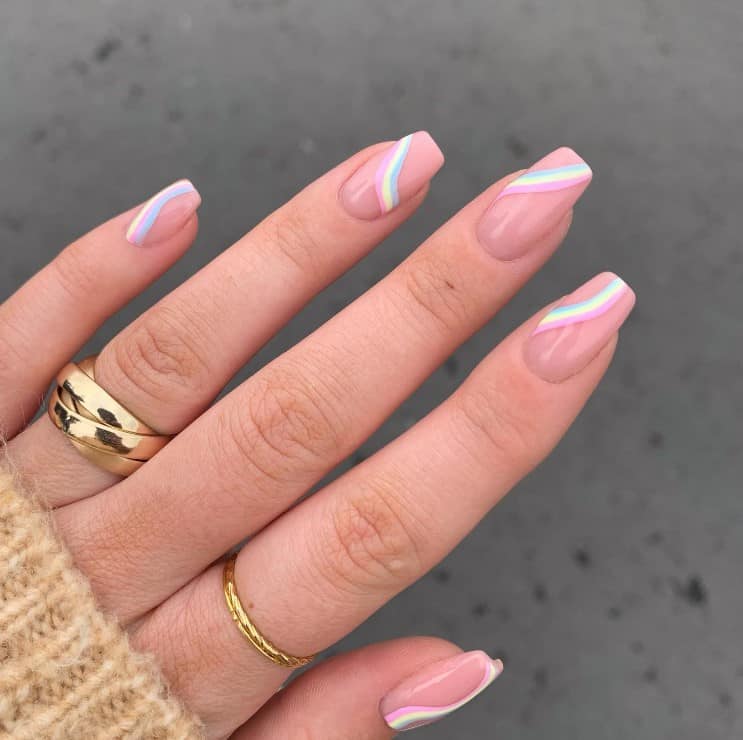 A woman's fingernails with a glossy nude nail polish that has rainbow-inspired diagonal French tips
