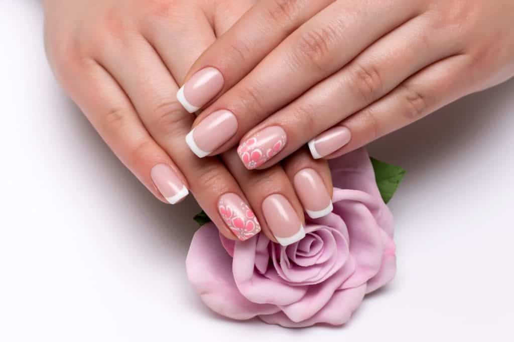 A closeup of a woman's fingernails with a nude nail polish that has white nail tips and painted cherry blossom on select nails 