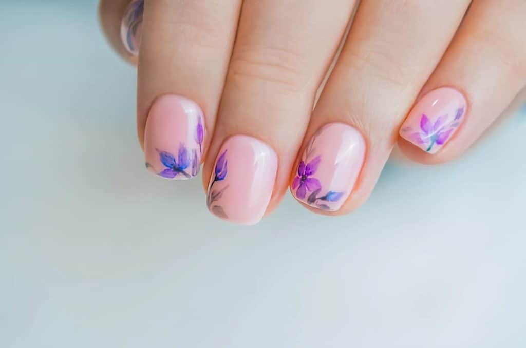 A closeup of a woman's fingernails with a light pink nail polish that has oriental flowers near the tips using bright blue and purple colors
