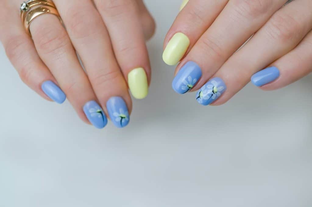 A woman's fingernails with pistachio green and icy blue nail polish that has flower art on select nails 