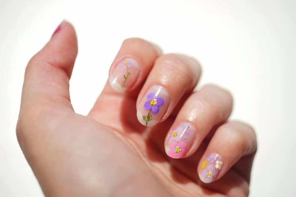 A closeup of a woman's fingernails with a nude nail polish that has various and multicolored flower art on each nail