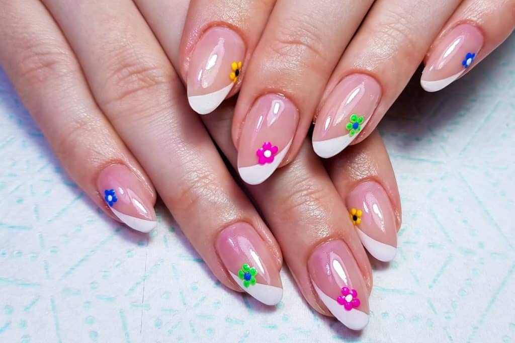 A closeup of a woman's fingernails with a glossy nude nail polish that has white French tips and different-colored flowers to each nail