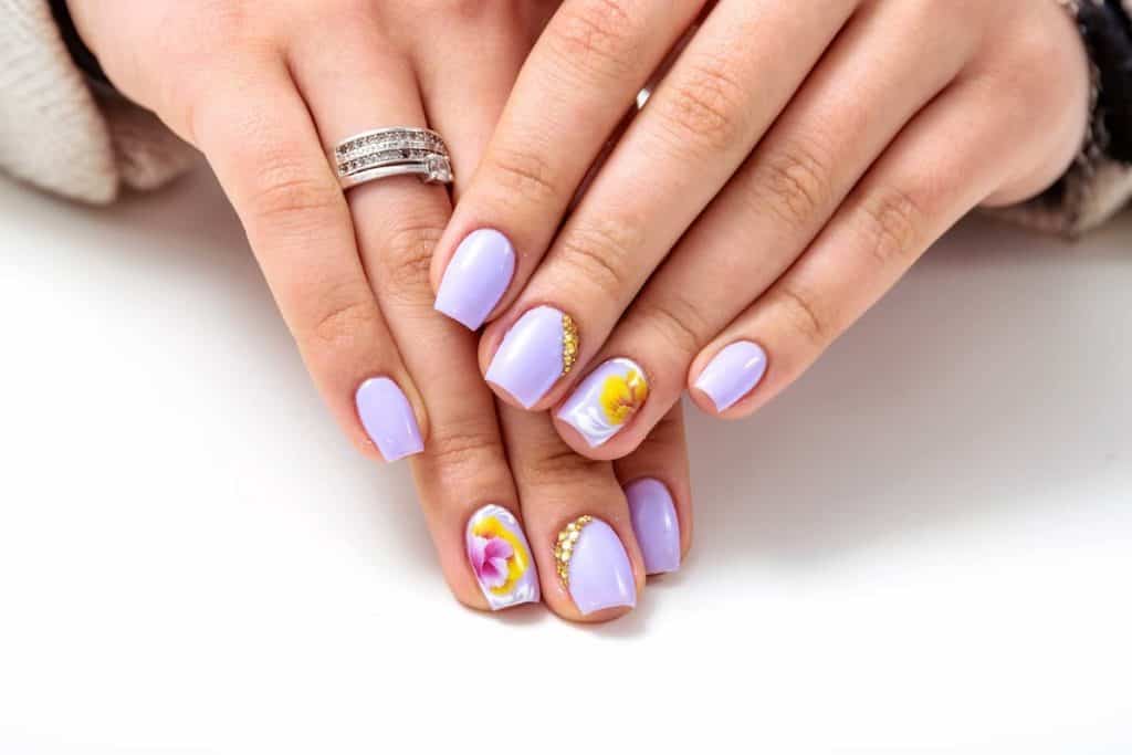 A woman's fingernails with a lavender nail polish base that has diamonds on one nail and a flower design on the other