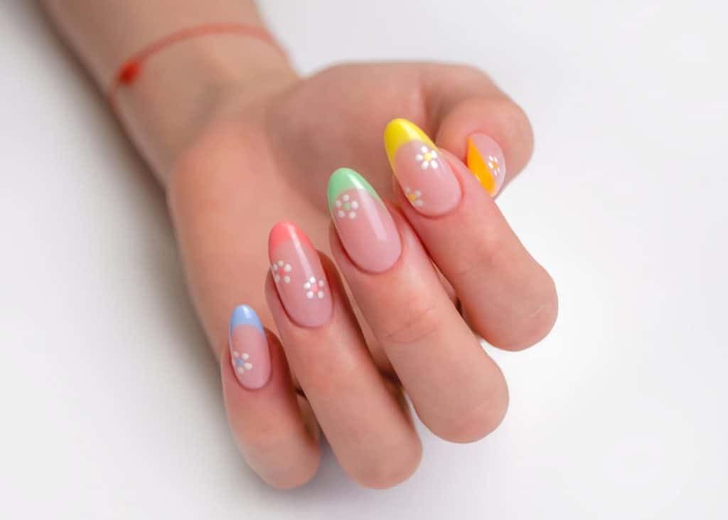 A woman's fingernails with a nude nail polish that has rainbow French tips and flowers nail designs