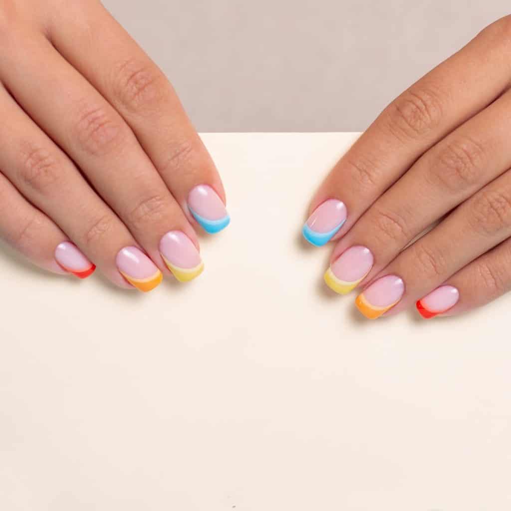 A woman's fingernails with a nude nail polish that has yellow, blue, red, and orange French tips