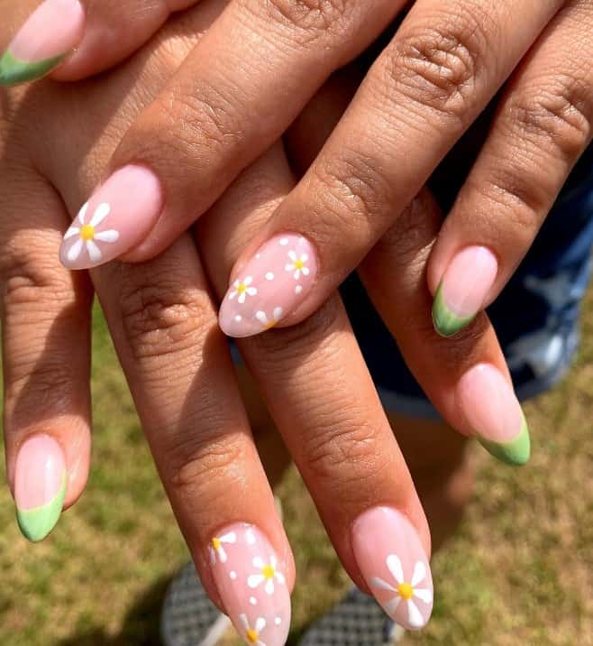 A closeup of a woman's fingernails with a nude nail polish that has white-and-yellow flowers and green-colored French tips