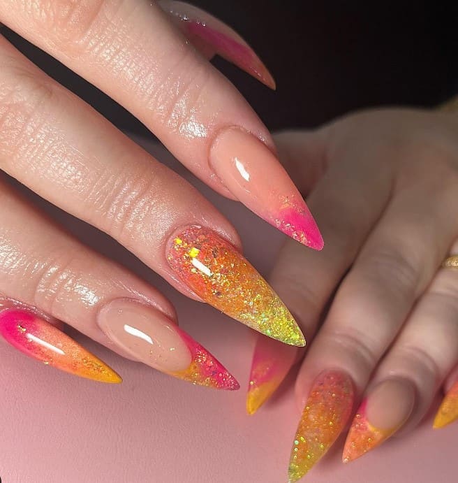 A closeup of a woman's fingernails with a peach-based nail polish base that has glitter designs in shades of pink and orange at the tips or covering the entire nail