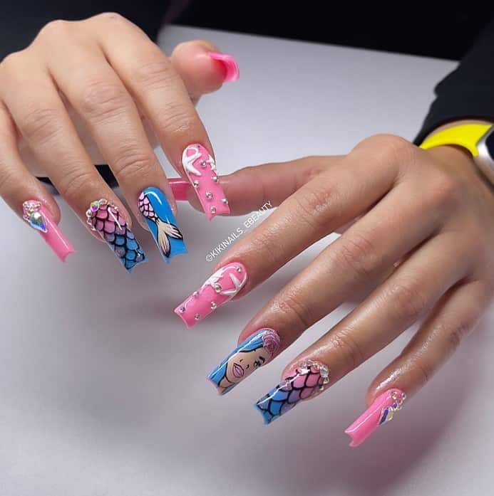 A woman's fingernails with a combination of blue and pink nail polish base that has rhinestones, scales, and mermaid nail art 