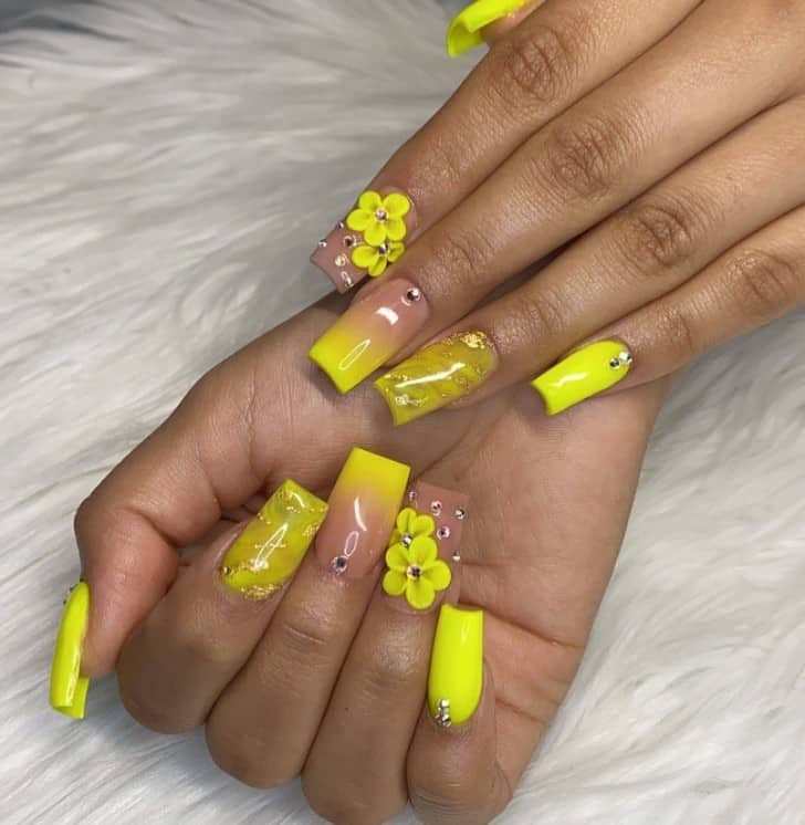 A woman's fingernails with a neon yellow nail polish base that has 3D flowers and rhinestones