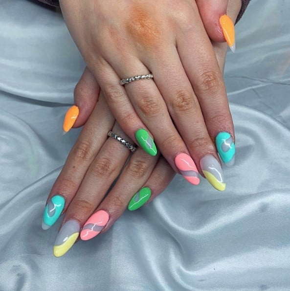 A closeup of a woman's fingernails with lively swirls in bright colors that has summer acrylic nails on almond shapes