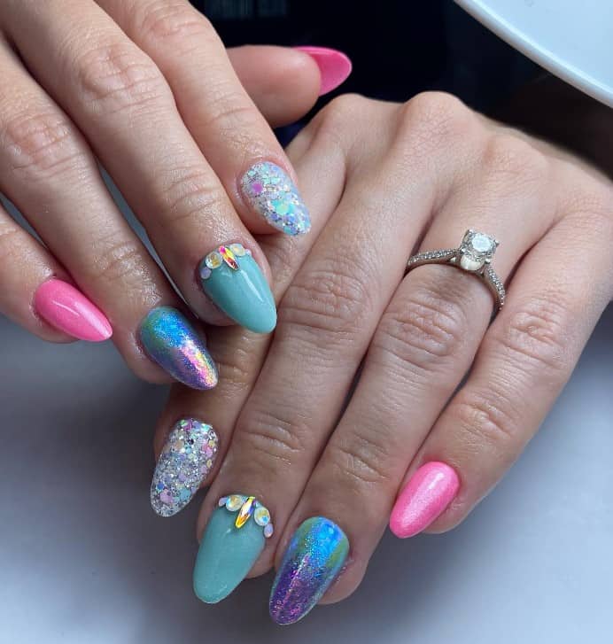 A closeup of a woman's fingernails with hues of blue, pink, and violet glitter that has Pearly rhinestones and chunky pastel glitter