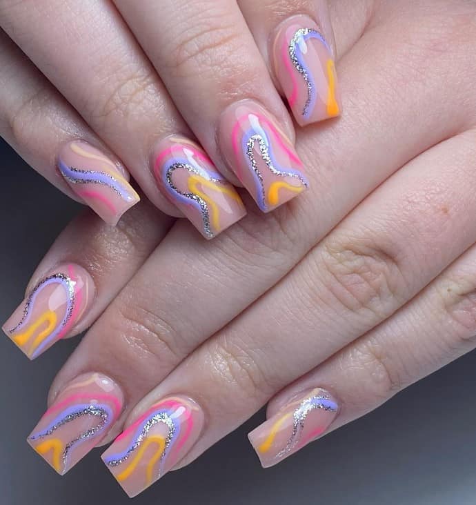 A closeup of a woman's short square fingernails with funky swirls of hot pink, blue, orange, and glittery silver that has peach base, creating a fun-filled look