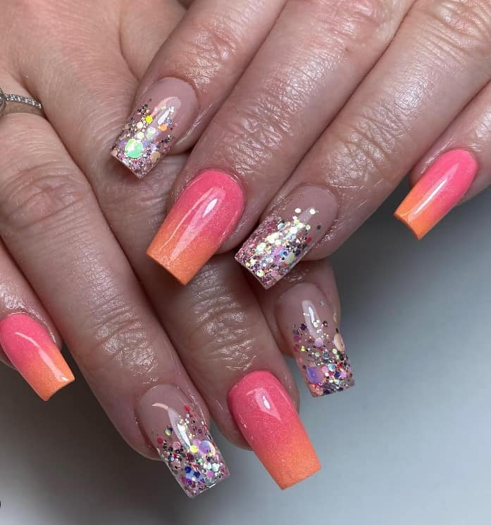 A closeup of a woman's perfect blend of brightness and elegance fingernails with a captivating ombré in orange to melon pink that has colorful chunky glitter tips on a nude base