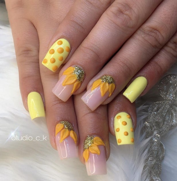 A closeup of a woman's fingernails with radiant yellow and orange hues that has sunflowers on cuticles, solid light yellow nails, and yellow nails with orange polka dots