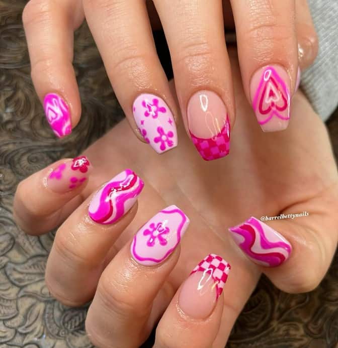 A closeup of a woman's fingernails with a pink and magenta nail polish base that has swirling patterns to blooming flowers, beaming hearts, and checkered tips