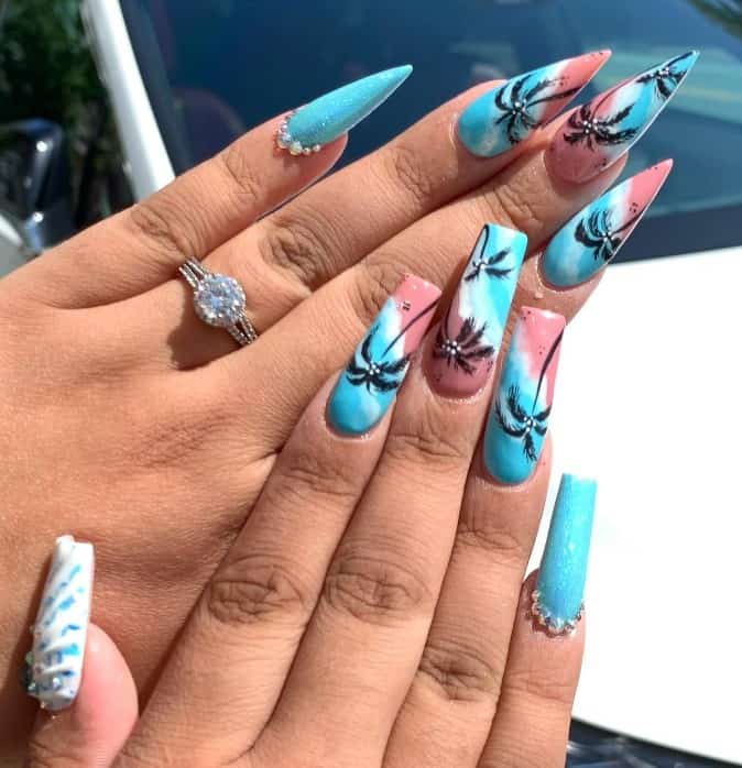 A closeup of a woman's fingernails with a baby blue base that has touches of light pink and white mimic sandy shores and palm tree art