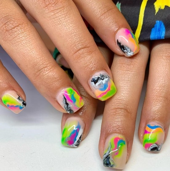 A closeup of a woman's fingernails with a light peach base that has abstract neon and black and white splashes