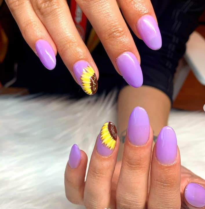 A closeup of a woman's fingernails with a purple nail polish base that has half-sunflower art