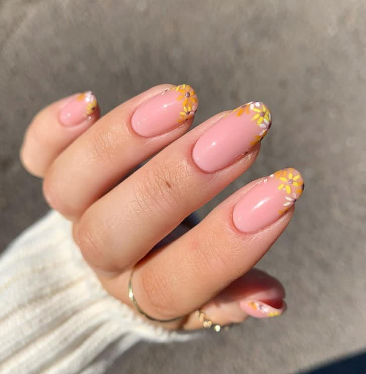 A woman's fingernails with a pale pink nail polish base that has tiny sunflowers French nail tips 