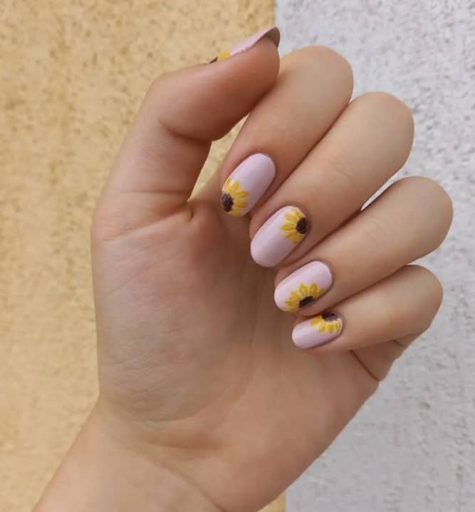 A woman's fingernails with a nude nail polish base that has a beautiful sunflower nail designs on each nail