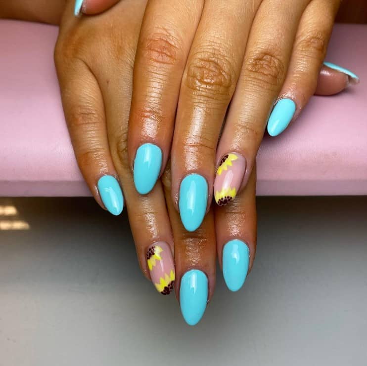 A woman's fingernails with a nude and baby blue nail polish base that has sunflowers on top of one nude-colored nail each hand