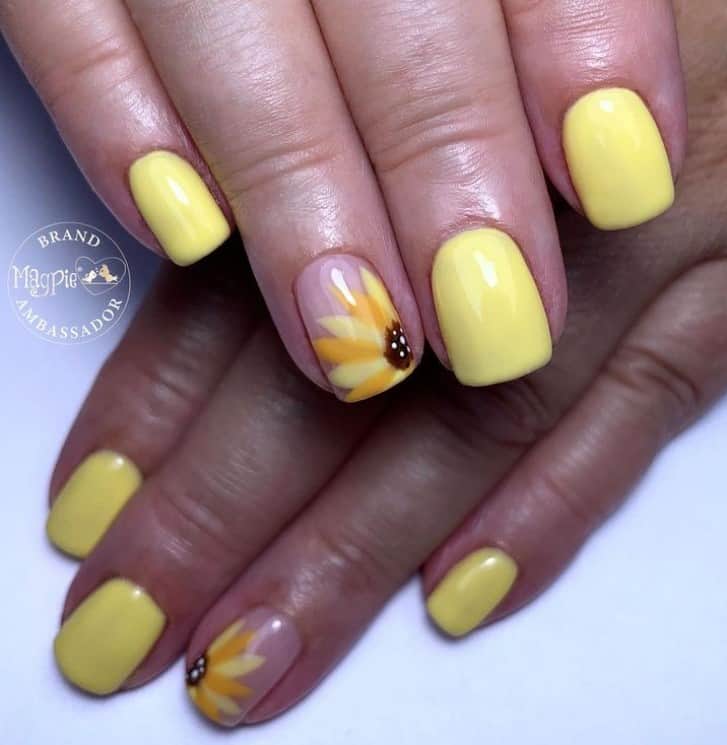 A closeup of a woman's fingernails with a mix of nude and yellow nail polish base that has simple sunflower accent on select nails 