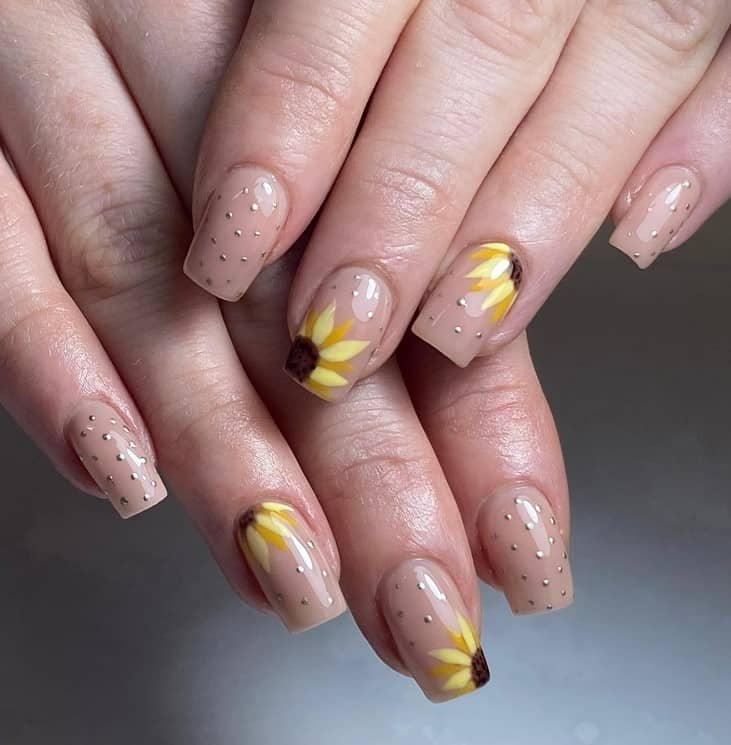 A closeup of a woman's fingernails with a nude nail polish base that has glittery polka dots and two sunflower nail accents