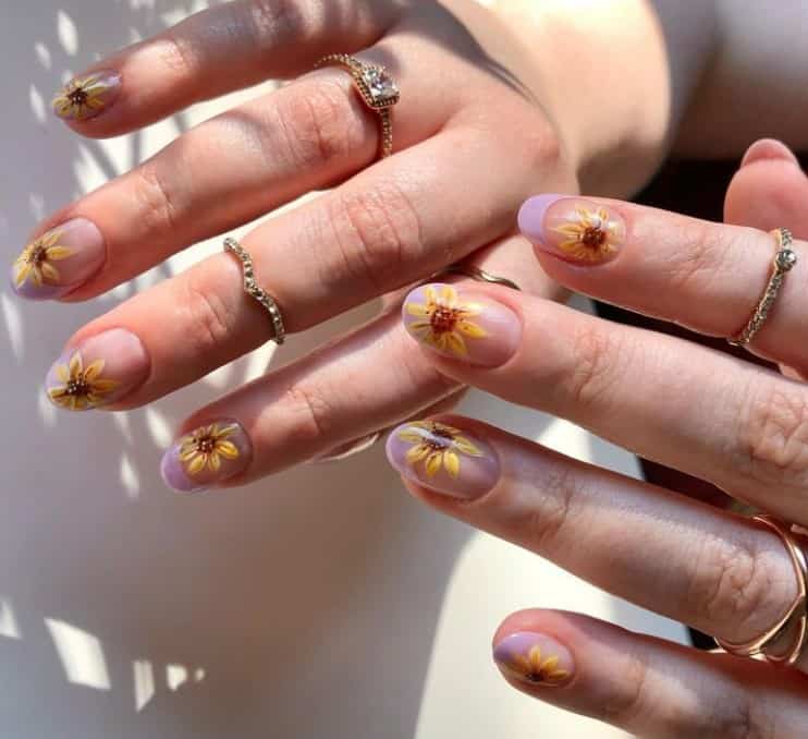 A closeup of a woman's fingernails with a nude nail polish that has sunflowers design on each nail and purple French tips