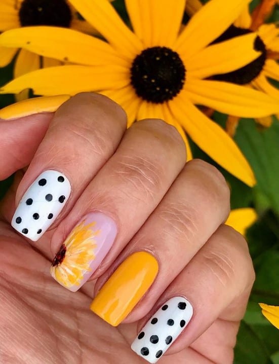 A closeup of a woman's fingernails with white, nude and yellow nail polish that has polka dot and sunflower design
