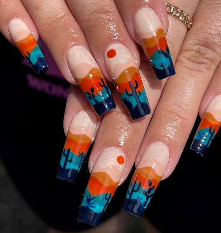 A closeup of a woman's fingernails with a nude nail polish that has desert landscape in Southwestern-inspired color palette nail designs