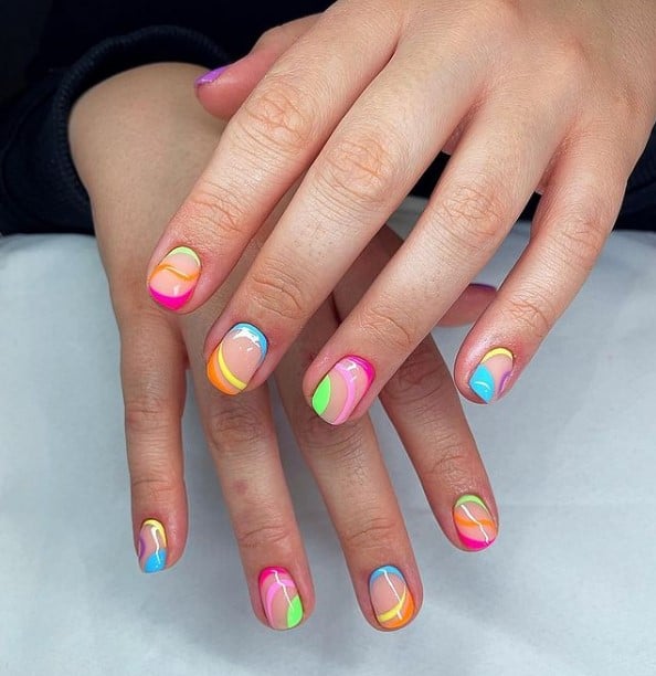 A closeup of a woman's fingernails with a nude nail polish that has bright and bold neon colors on nail tips 