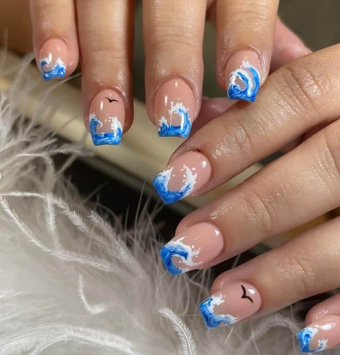 A closeup of a woman's fingernails with a nude nail polish that has ocean waves and seagulls nail designs