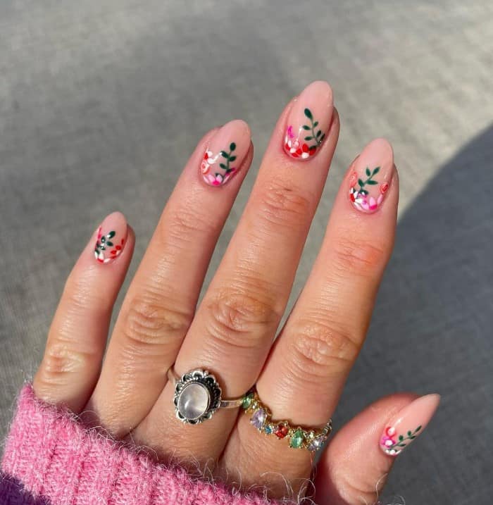 A woman's fingernails with a pale pink nail polish that has orange and hunter green flowers and leaves