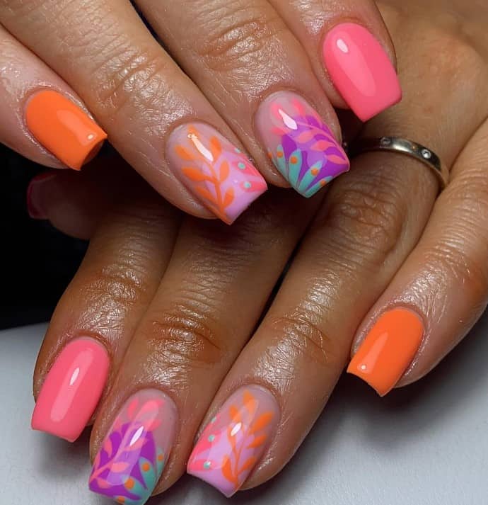 A closeup of a woman's fingernails with a multicolored nail polish that has matte or glitter finishes and floral nail art 