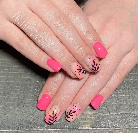A closeup of a woman's fingernails with a different shades of pink nail polish that has black leaf nail art on select nails 