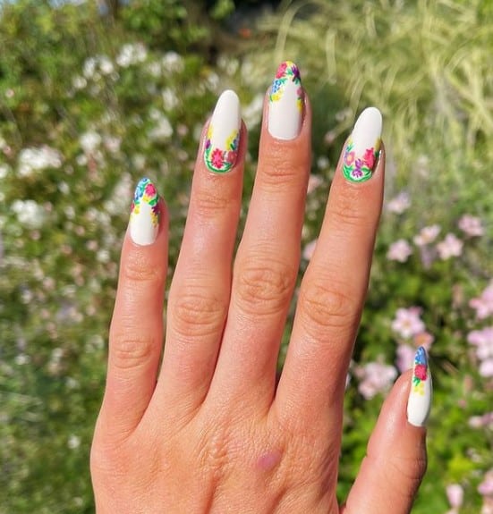 A woman's fingernails with a white nail polish that has florals on the tips and cuticles