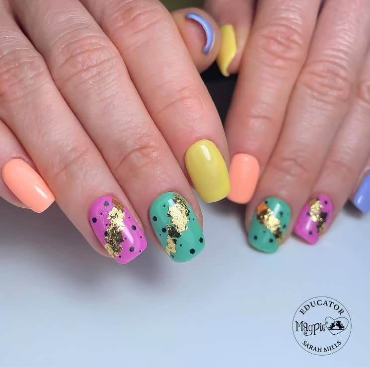 A closeup of a woman's fingernails with a multicolored nail polish that has gold foil details and black accents