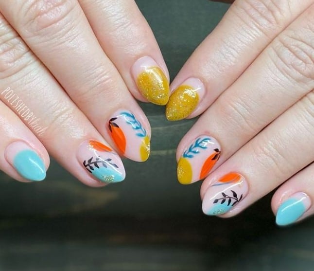 A closeup of a woman's fingernails with a nude nail polish that has abstract shapes, gold and blue nail tips, and leaves nail designs 