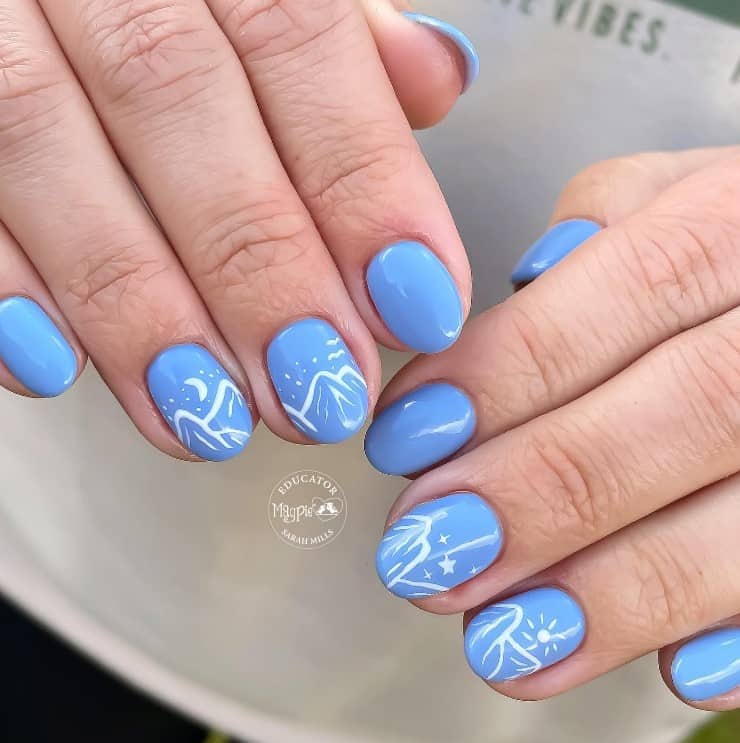 A closeup of a woman's fingernails with powder blue manicure that has white mountainscape on select nails