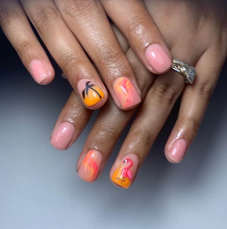 A closeup of a woman's fingernails with glossy orange-and-pink nail polish that has palm tree, flamingo, and marbly swirl designs