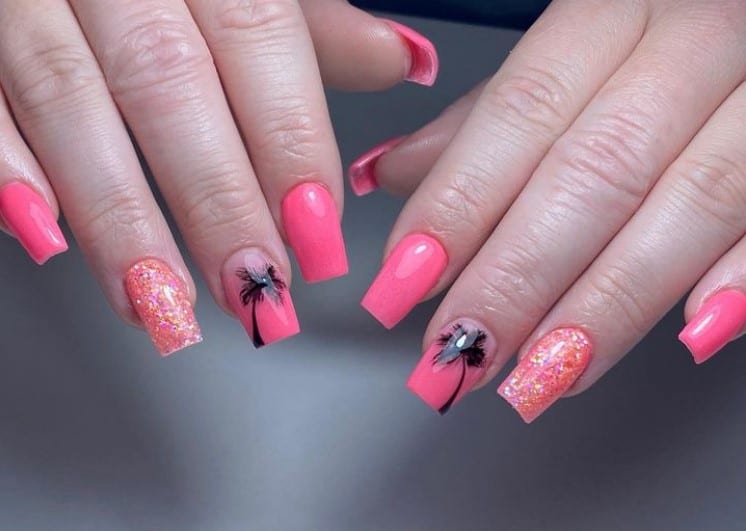 A closeup of a woman's fingernails with a pink nail polish base that has glittery accent nails and palm tree nail art