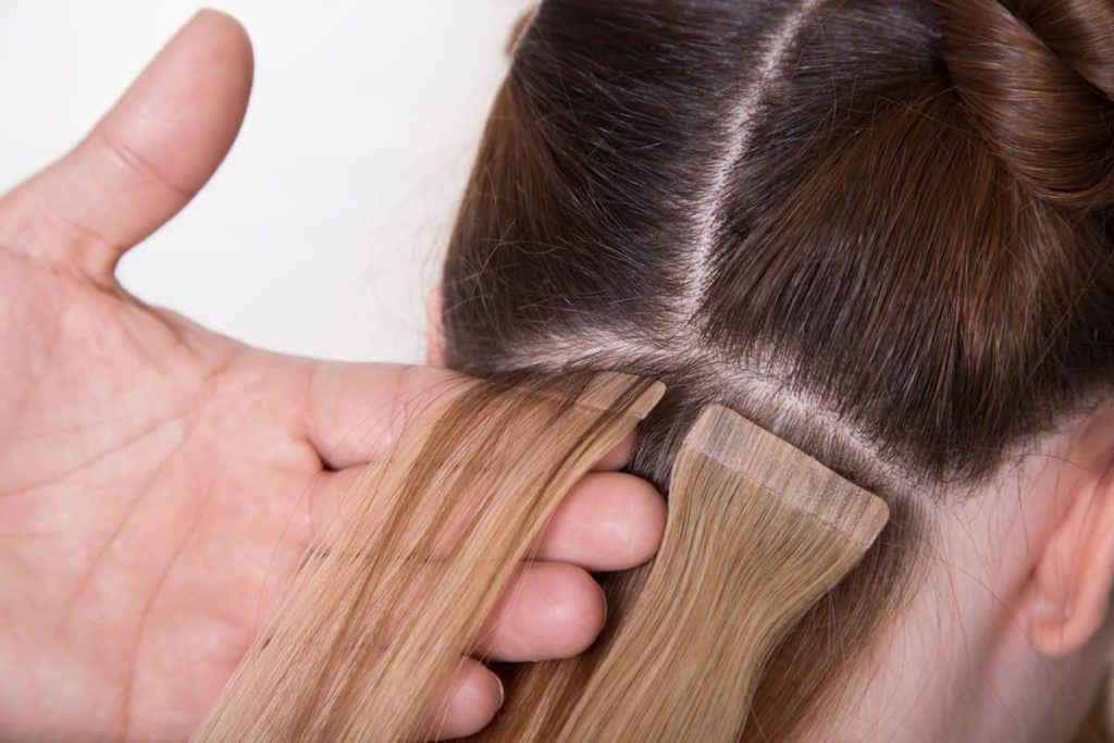 A blonde tape in hair extension being applied on woman's hair